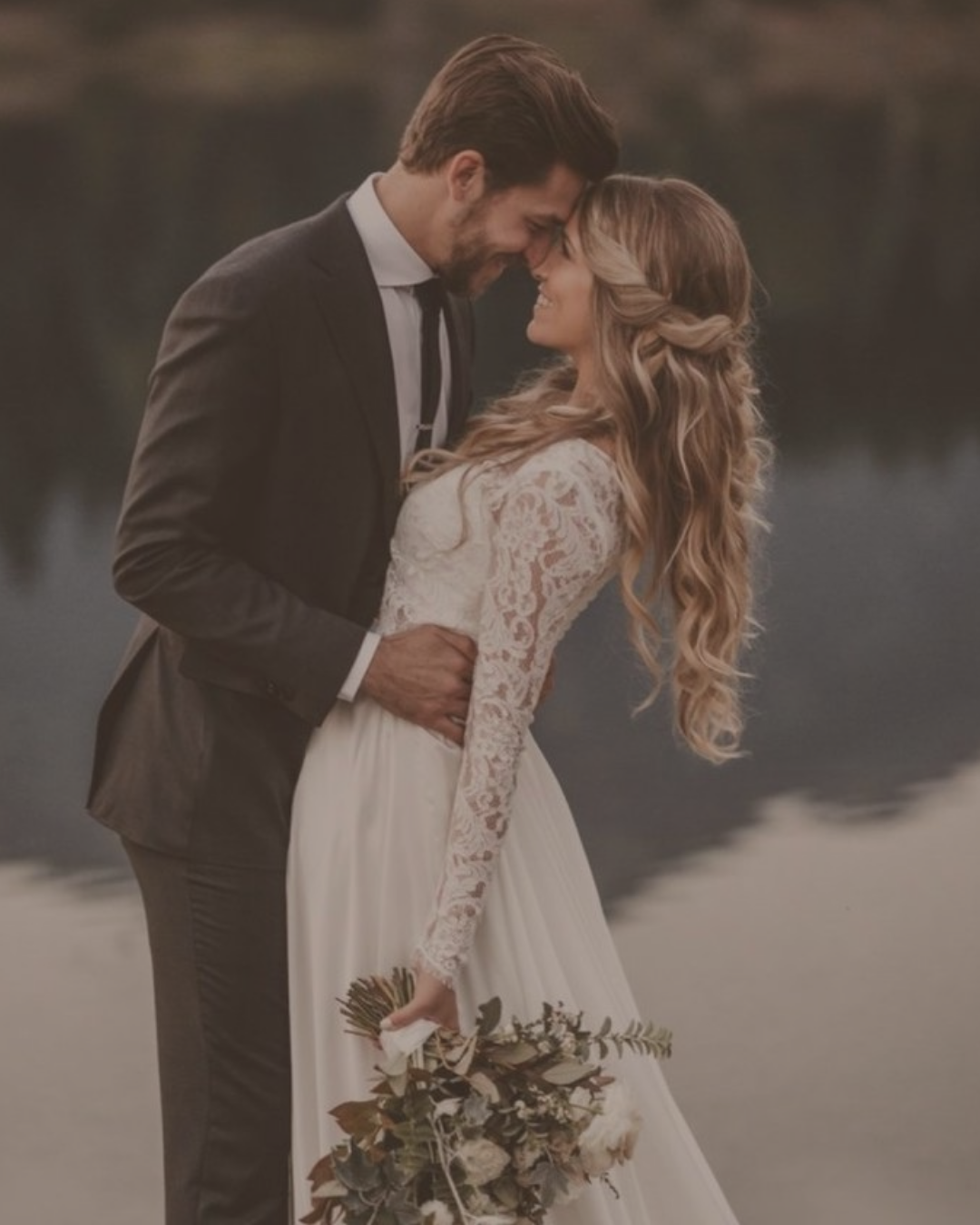 A bride and groom in a warm, sepia-toned portrait — foreheads touching, smiling